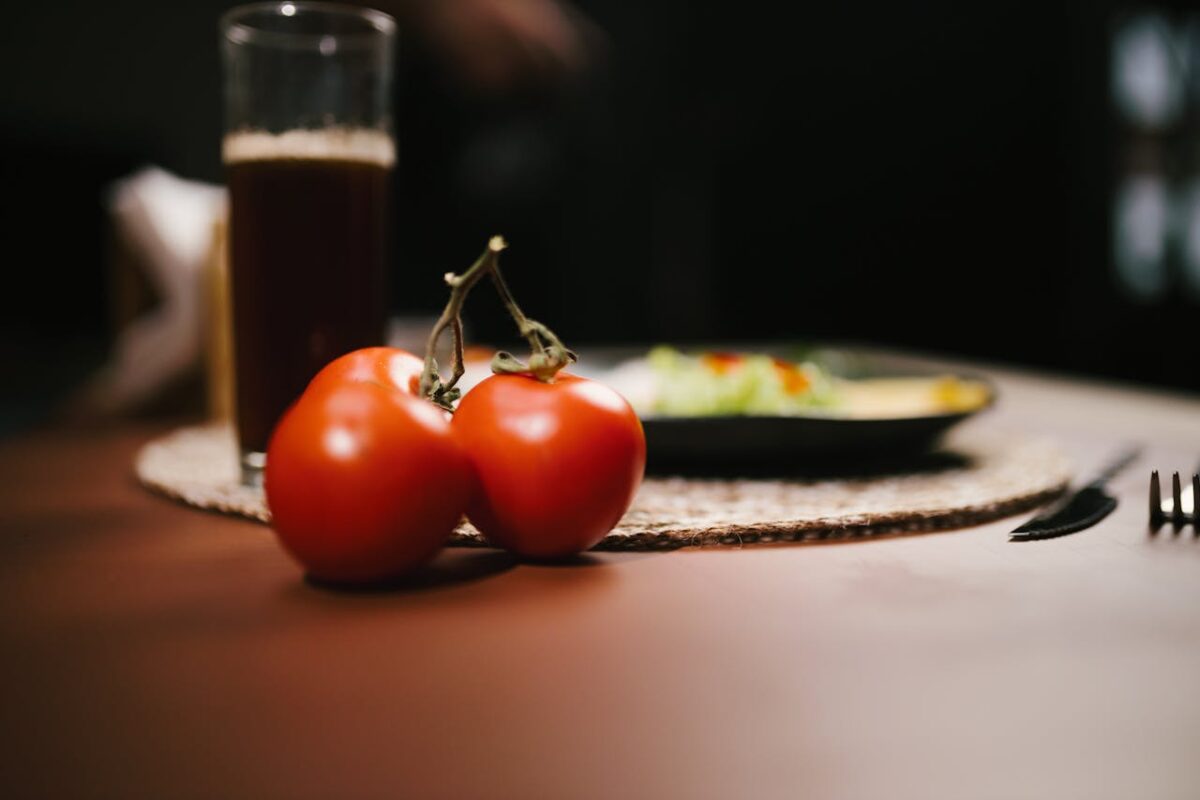 Close-up of ripe tomatoes with a glass of juice and salad plate in a cozy dining setting.