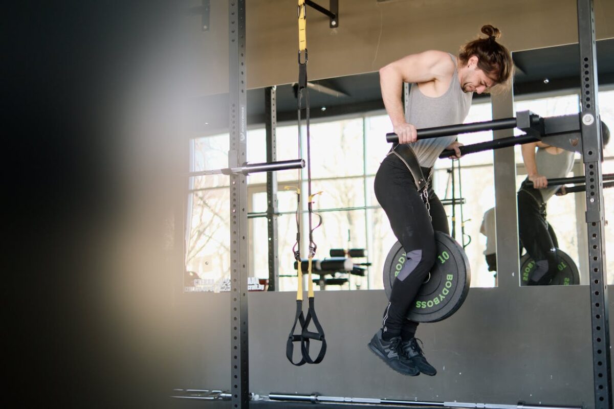 Fit man performing weighted pull-ups in a gym setting, showing strength and determination.